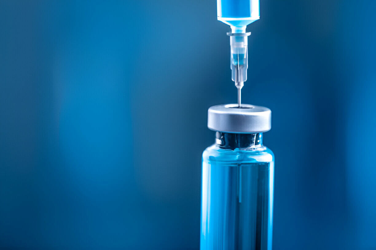 A syringe drawing a dose from a glass vial